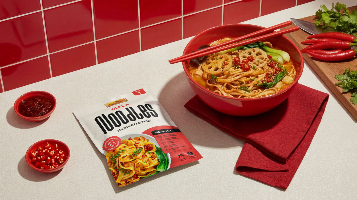 Mala Noodles Sichuan Style meal kit packet beside a red bowl of spicy noodle soup with lotus root, bok choy, and chillies | Brand & Packaging Design by Deuce Studio London