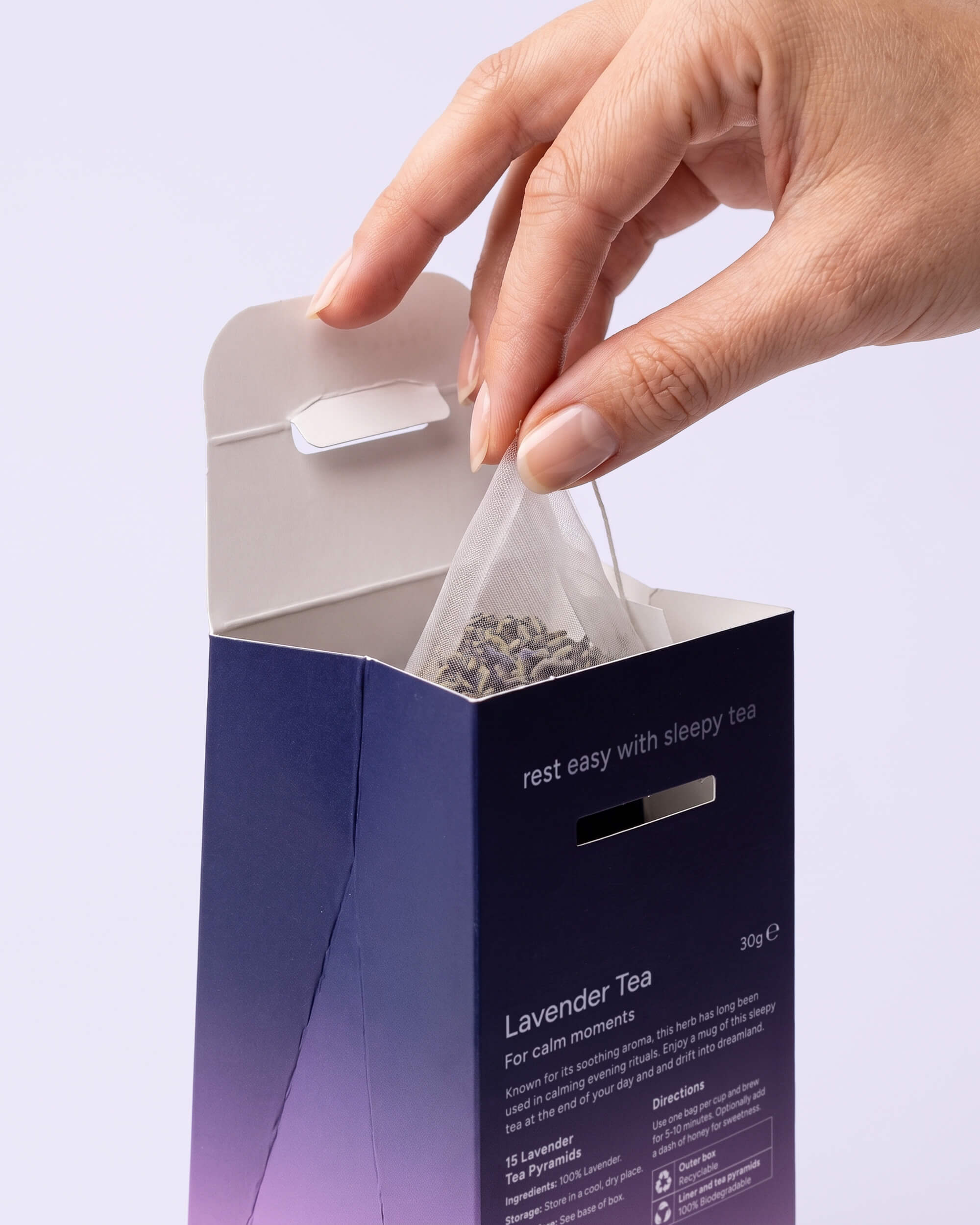 Hand lifting a lavender pyramid teabag from an open Cydno carton reading 'rest easy with sleepy tea'