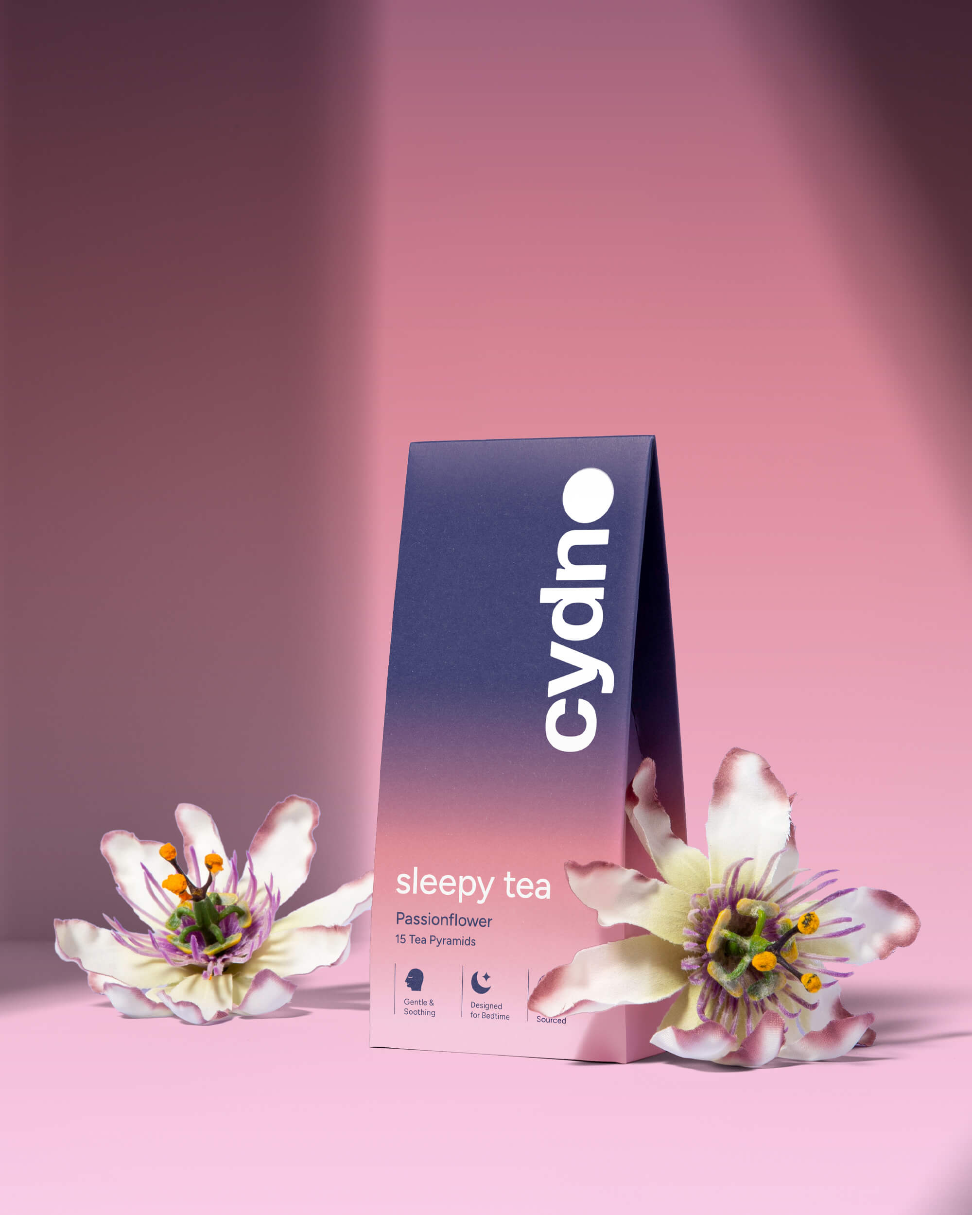 Cydno Passionflower sleepy tea carton in a navy-to-peach gradient, flanked by two real passionflowers