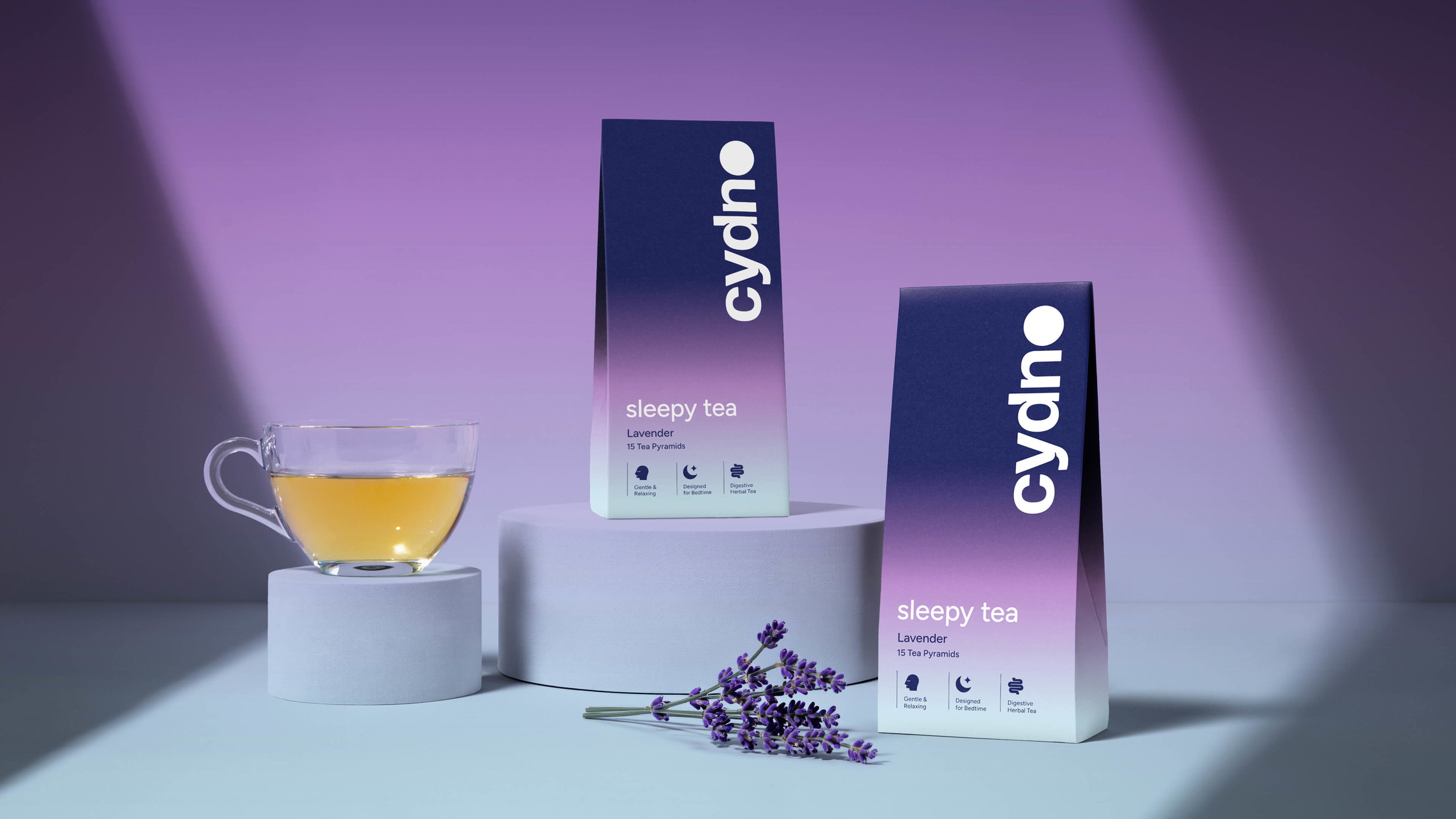 Two Cydno Lavender sleepy tea cartons beside a glass of amber tea and a fresh lavender sprig